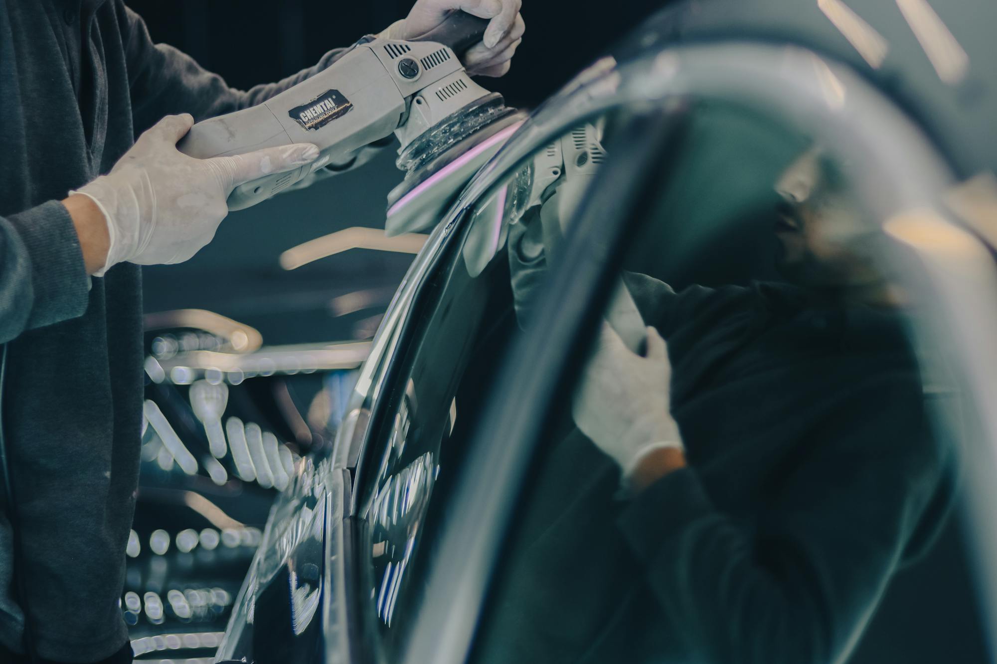 A detailer using a dual-action polisher on a glossy dark vehicle panel — the paint-correction prep step that determines whether a ceramic coating actually performs as advertised.