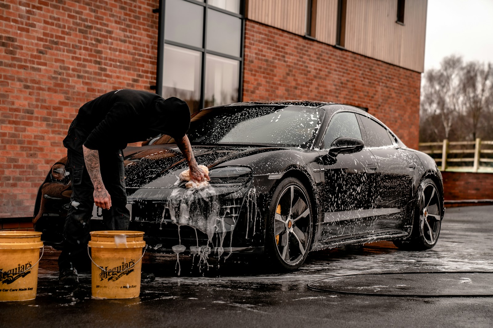A professional detailer polishing the hood of a luxury car under bright shop lighting.