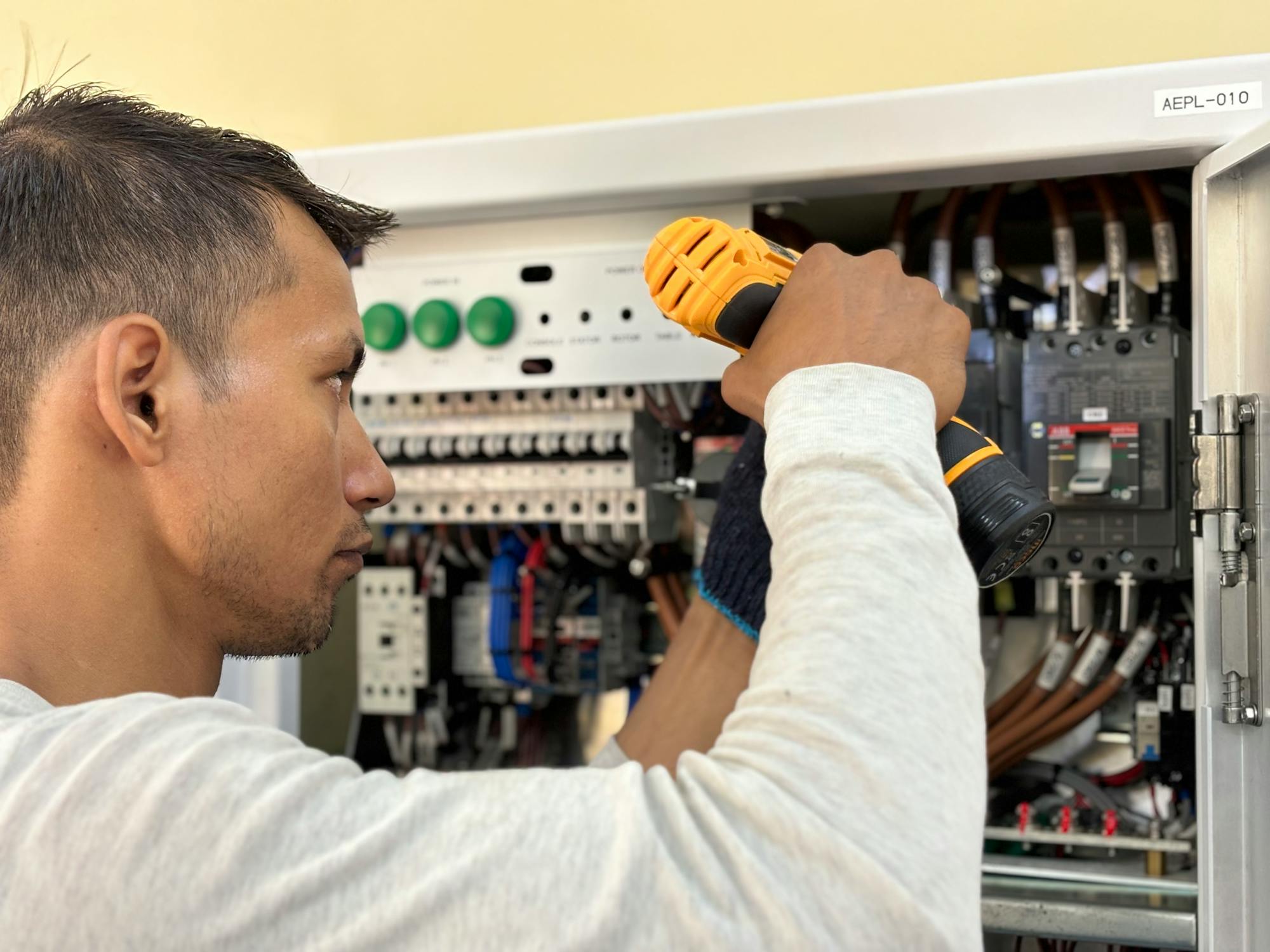 An electrician working with a power drill on a residential electrical panel during an EV charger install — the kind of code-compliant Level 2 work (NEC 625.42, 125% continuous load) that defines the $1,200-$3,000 high-margin install ticket in 2026.
