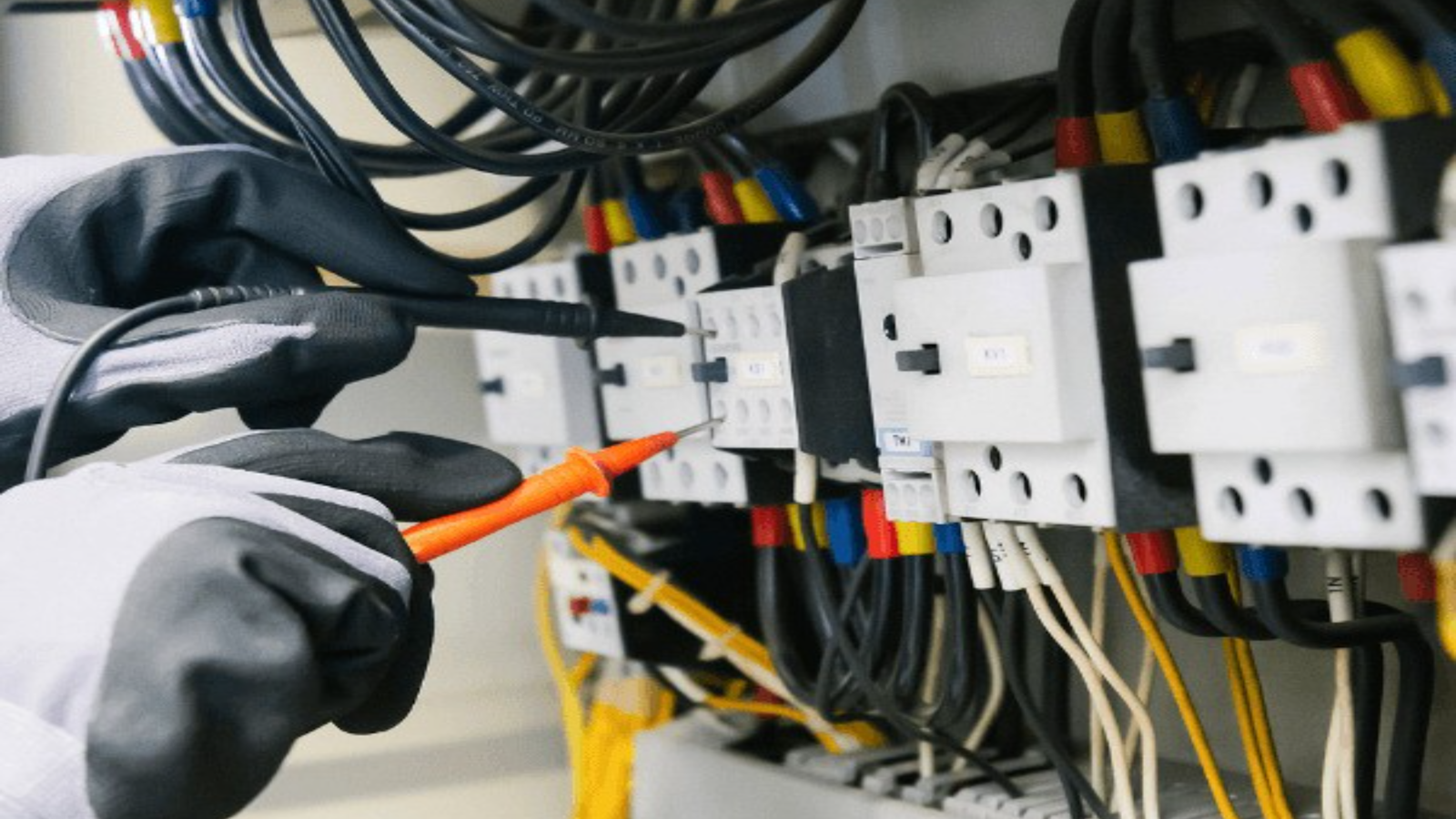 An electrician working on a residential electrical panel with breakers exposed and a multimeter in hand.