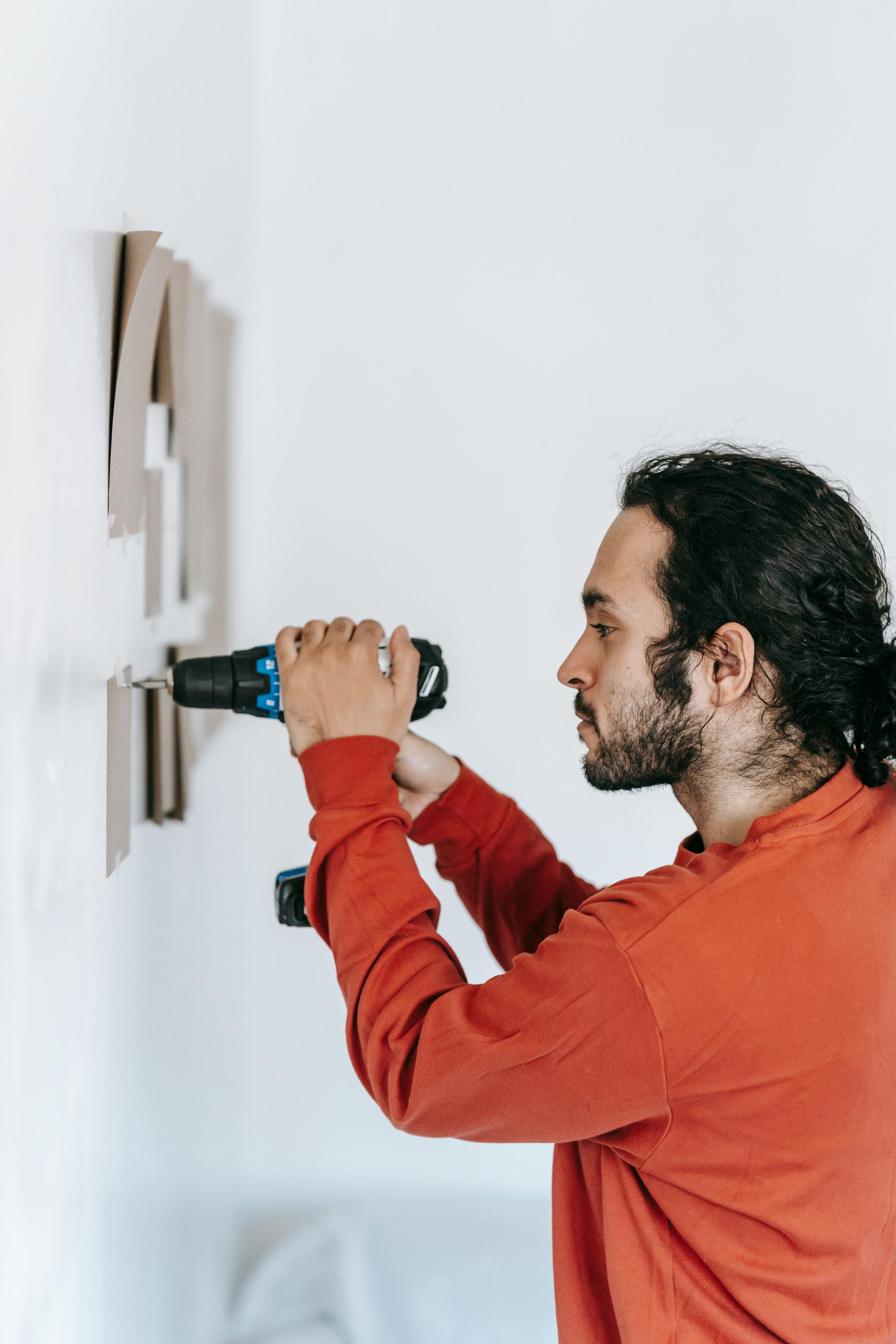 A handyman using a cordless drill on a residential wall during an install — the kind of $100-$300 single-task work that, bundled into honey-do list half-day blocks ($200-$300) or full-day blocks ($400-$600), anchors a solo handyman business in 2026.