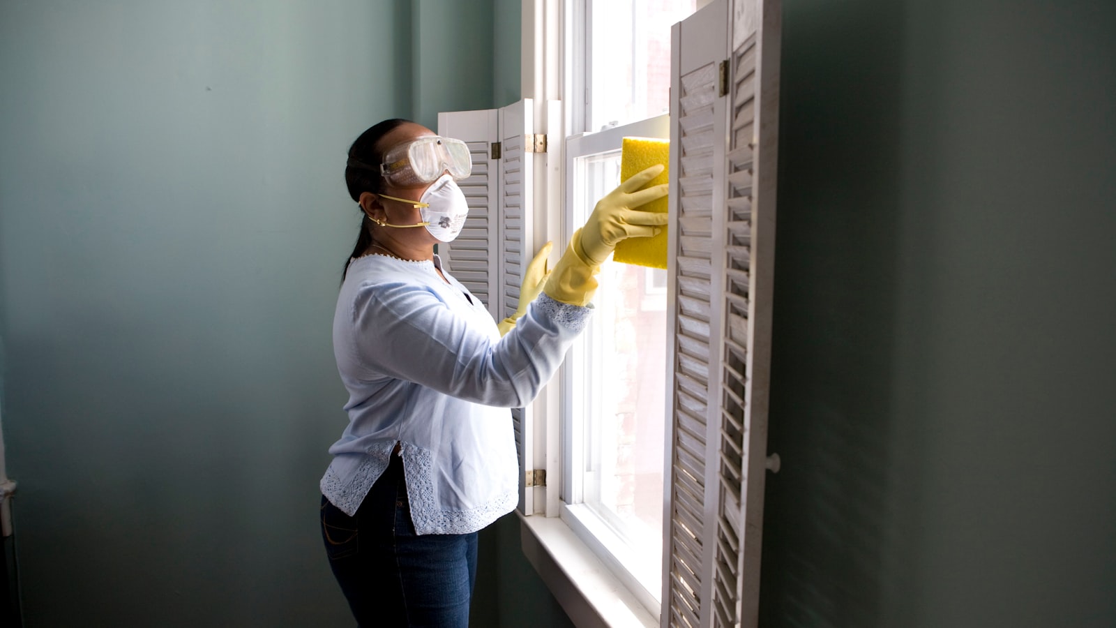 A residential cleaner using a microfiber cloth on a kitchen counter with cleaning supplies organized on the countertop.