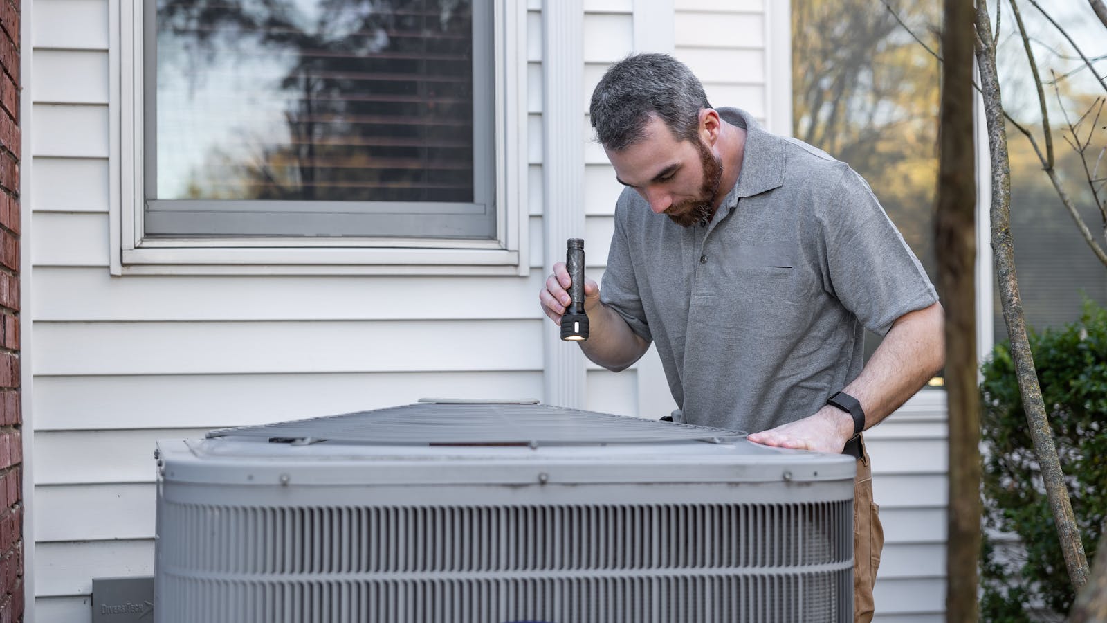 An HVAC technician servicing a residential outdoor condenser unit with refrigerant gauges connected.
