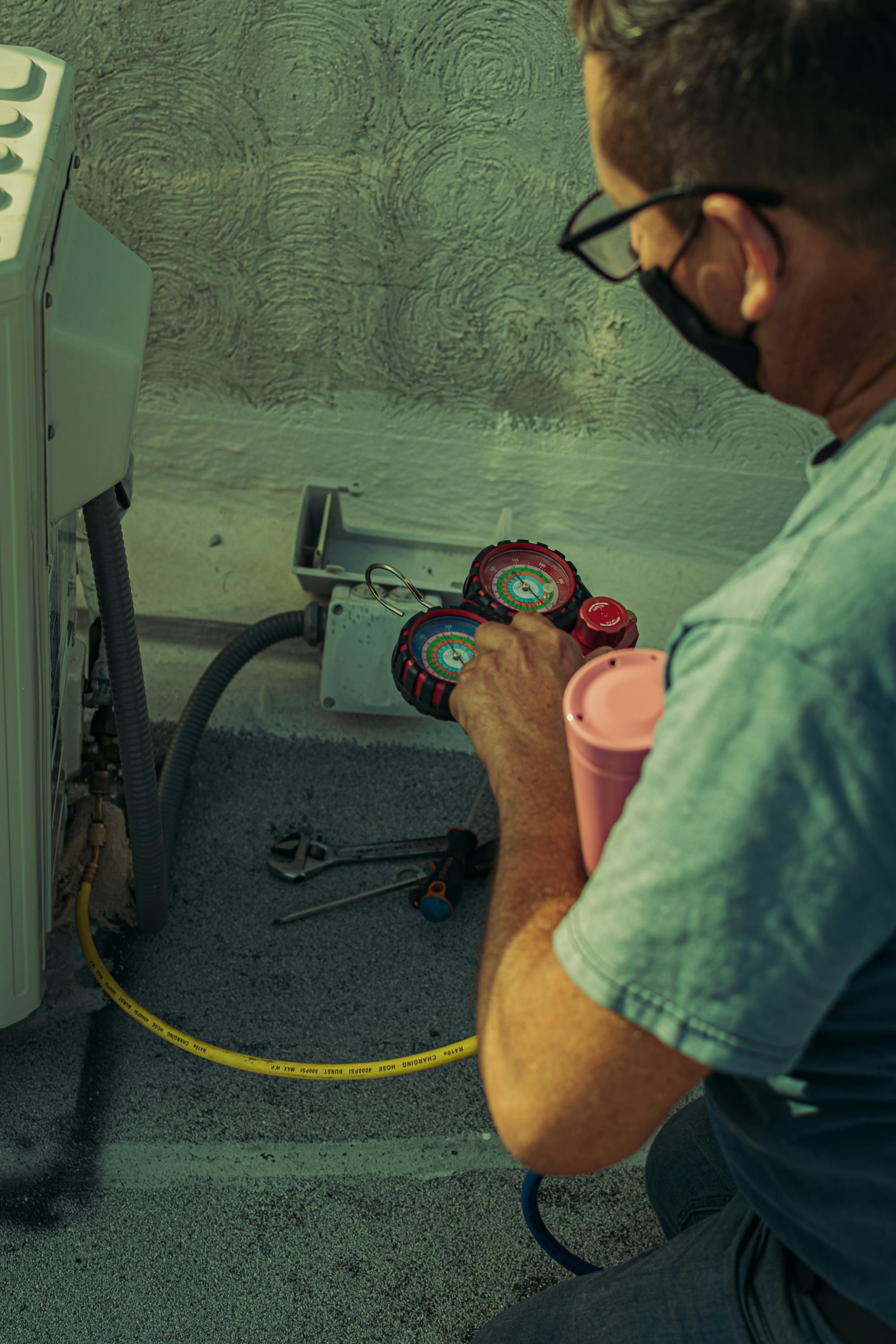 An HVAC technician using manifold gauges to check refrigerant pressures on an outdoor unit during a residential install — the kind of skilled equipment work that turns a service-call shop into a $7,500-$15,400 average-ticket install business in 2026.