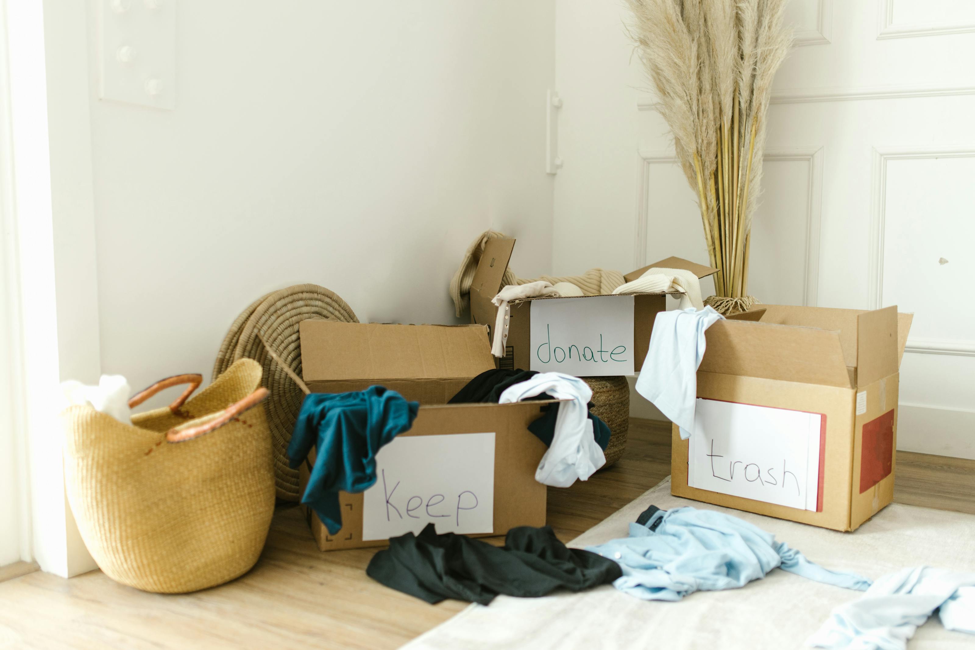 Cardboard boxes labeled Keep, Donate, and Trash filled with household items being sorted on a hardwood floor — the methodical sort-and-haul workflow at the core of both hoarder and estate cleanout work in 2026.