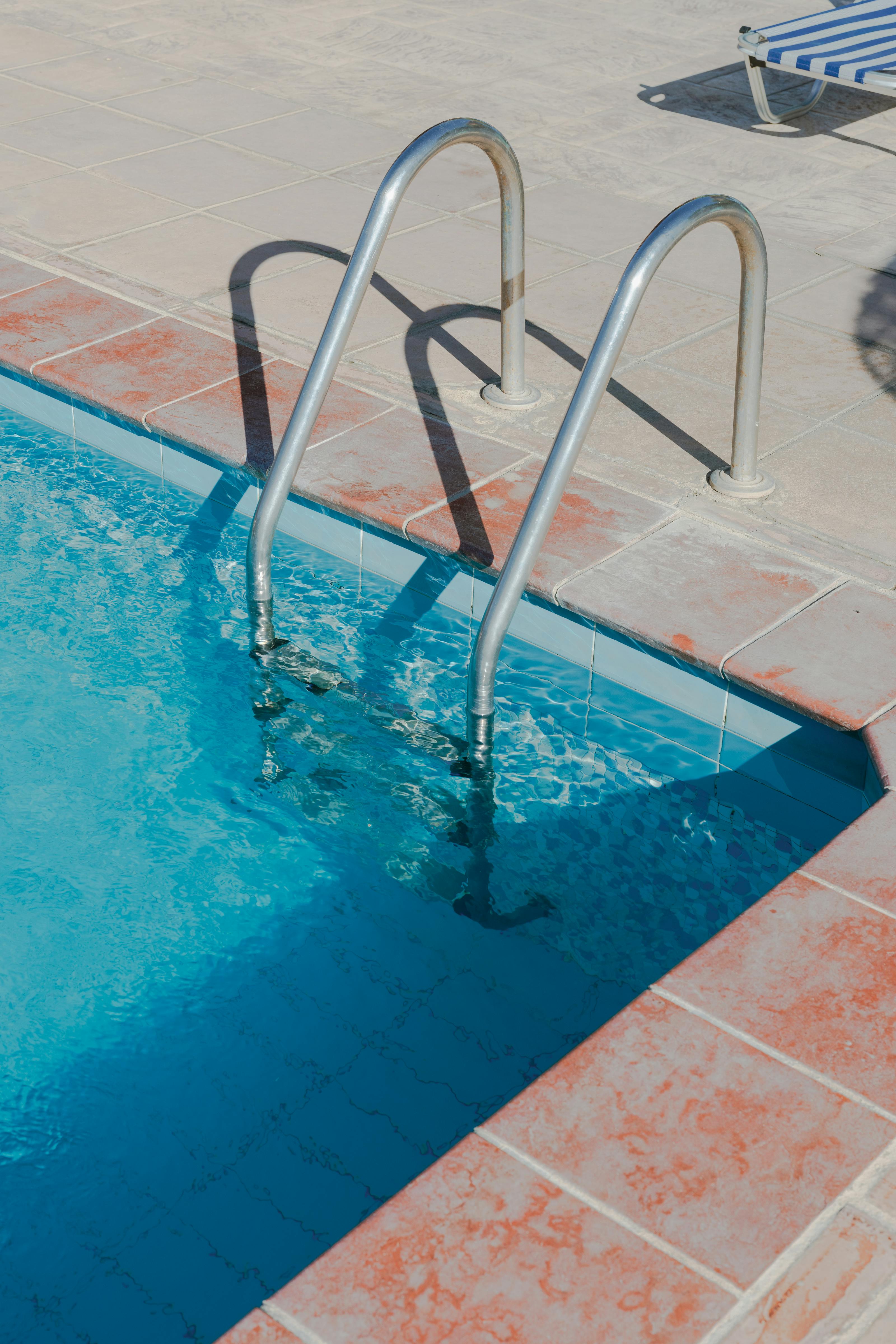 Stainless-steel pool ladder set into a tiled deck — the kind of installed pool hardware (ladders, plumbing, pumps, salt cells, heaters, automation) that drives equipment-side revenue 5-30× larger per job than chemical-only service.