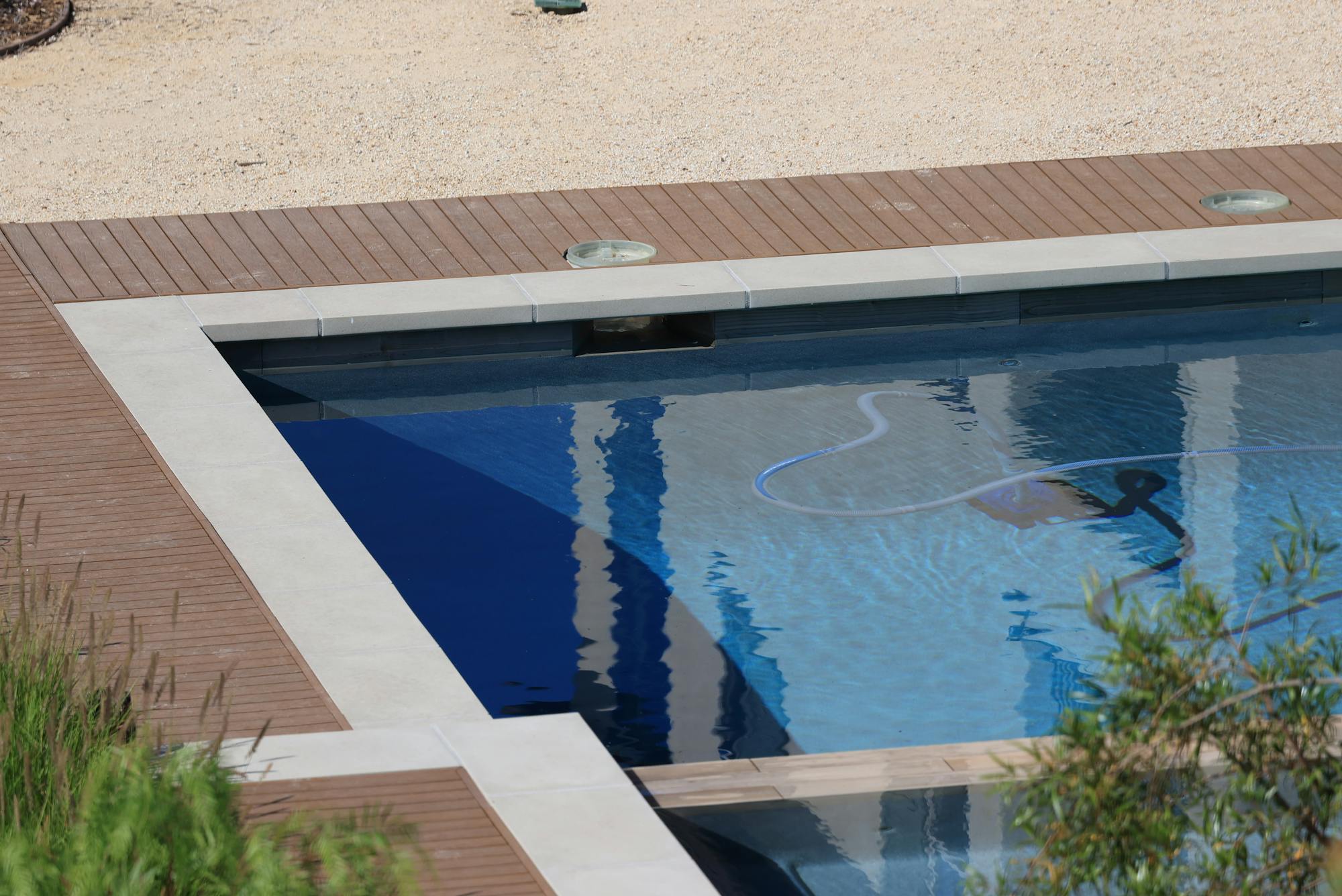 A residential swimming pool with a manual vacuum hose visible underwater during a routine service visit — the kind of weekly recurring chemical and skim work ($80-$190/mo per pool) that anchors a route-density-driven pool service business in 2026.
